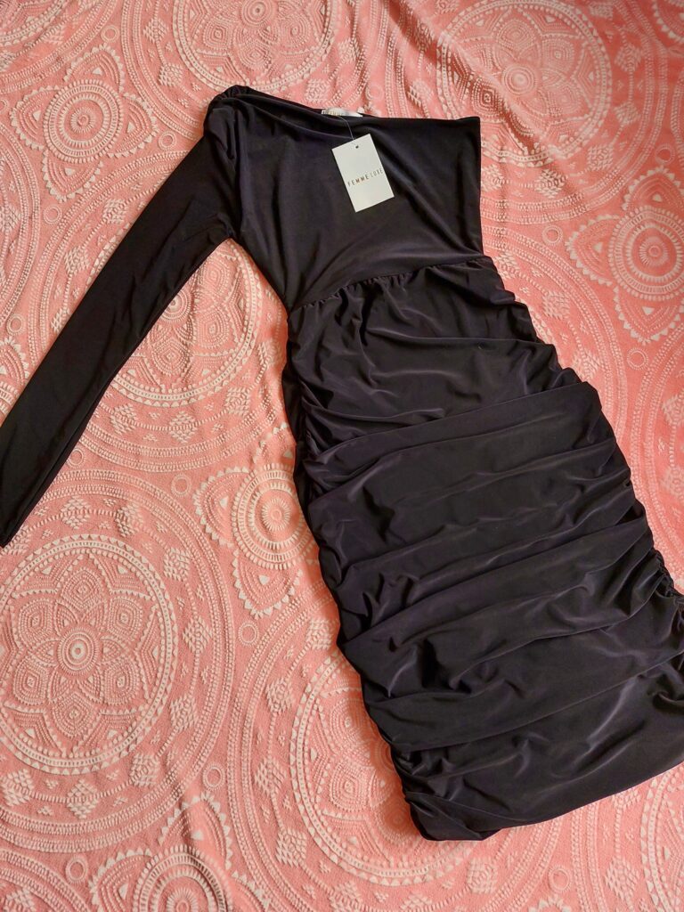 A flat lay of Black One Shoulder Ruched Slinky Dress. It shows the ruches that compliment the dress.