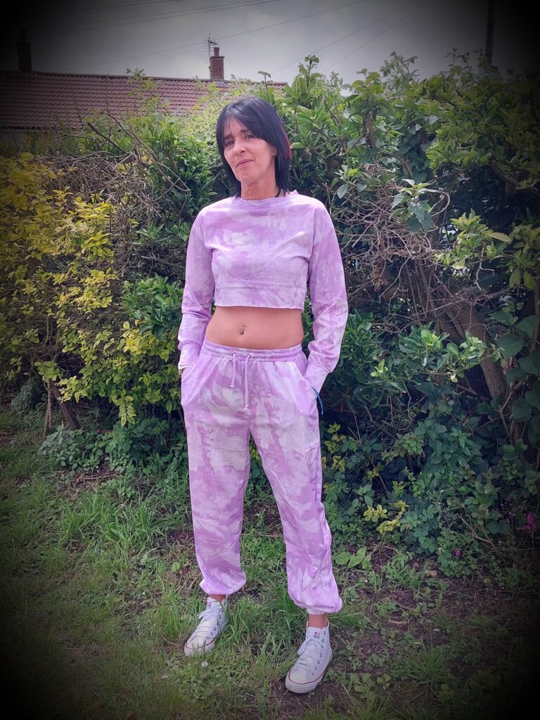 Lady wearing Purple Tie Dye Oversized Sweatshirt Co-ord. she is standing in front of a green shrub