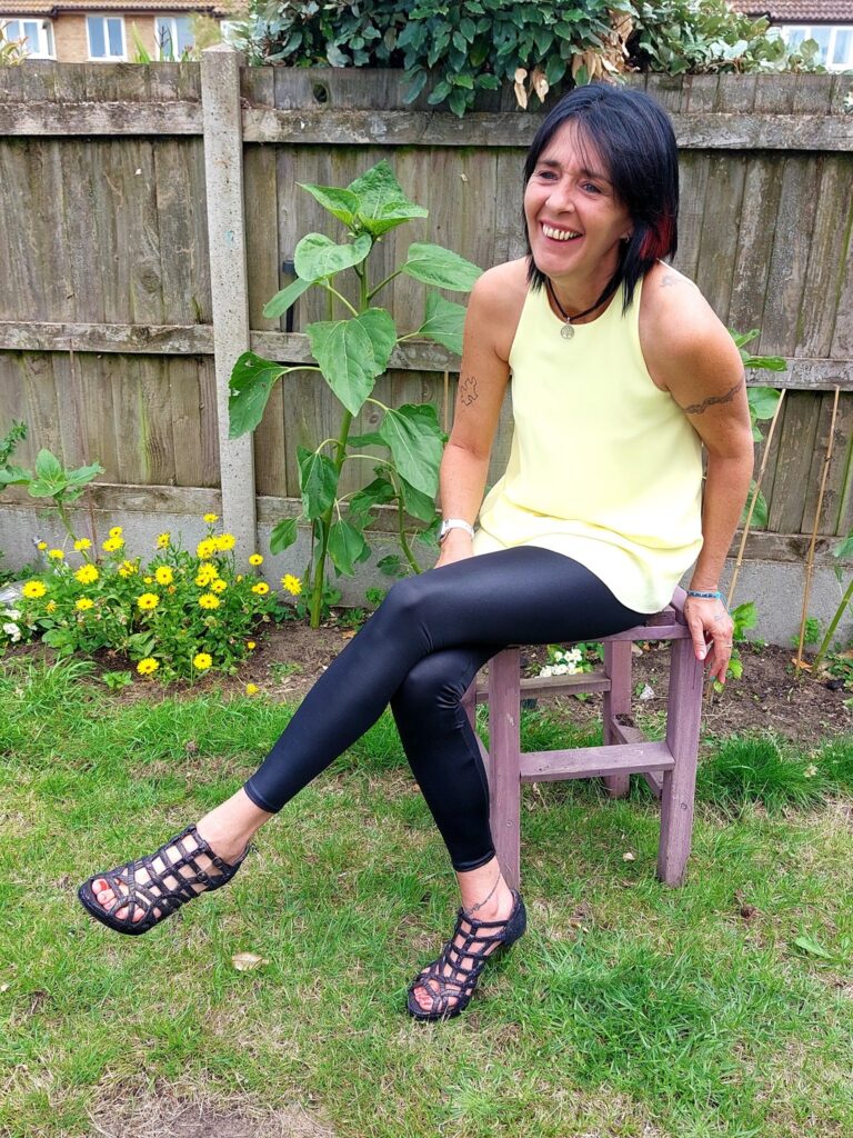 Lady wearing black leggings with a yellow blouse and high heels. She is sitting down on a purple stool