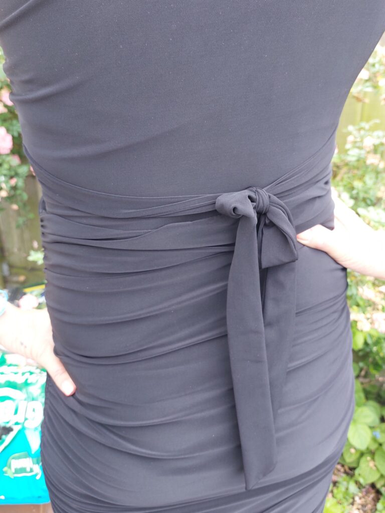 A back view of Black One Shoulder Ruched Slinky Dress showing the wrap belt and bow. it also shows the ruched material to compliment the dress