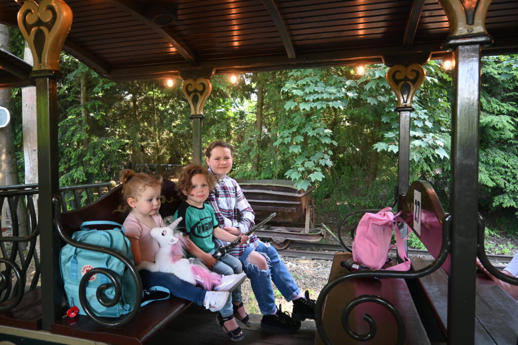 a teenager wearing ripped jeans, sitting on a steam train with 2 toddlers. One boy and one girl wearing pigtails at efteling theme park