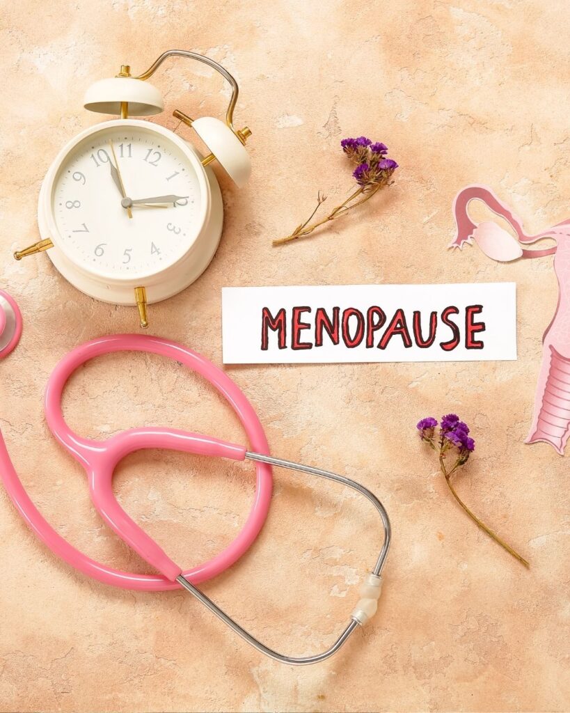 Flatlay image of an alarm clock, a stethoscope some red flowers and the word menopause