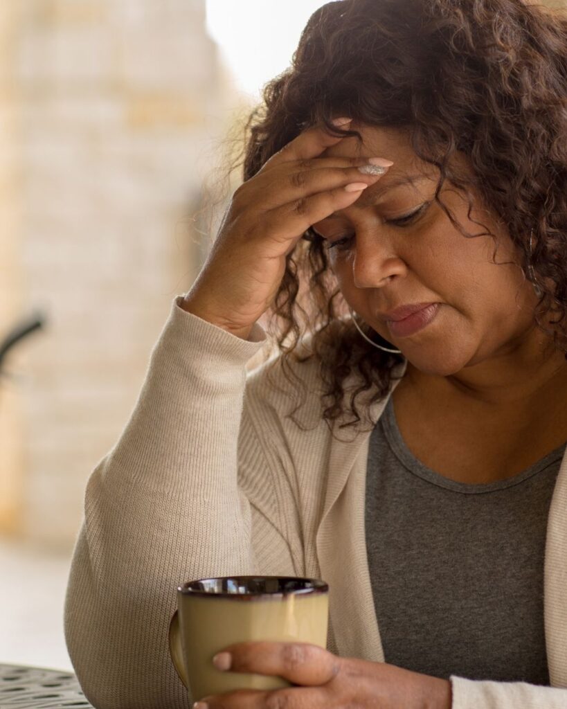 a middle aged lady with long dark curly hair with her hands in her head. she looks stressed and sad.
