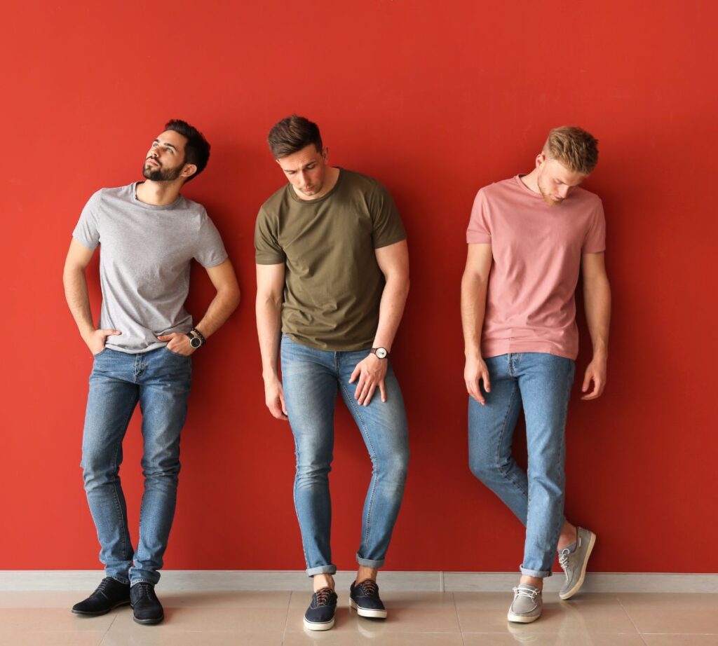 picture of three men each wearing a pair of blue denim jeans. One man wears a pink t-shirt with them. One man wears a khaki t-shirt. And one man wears a grey t-shirt.