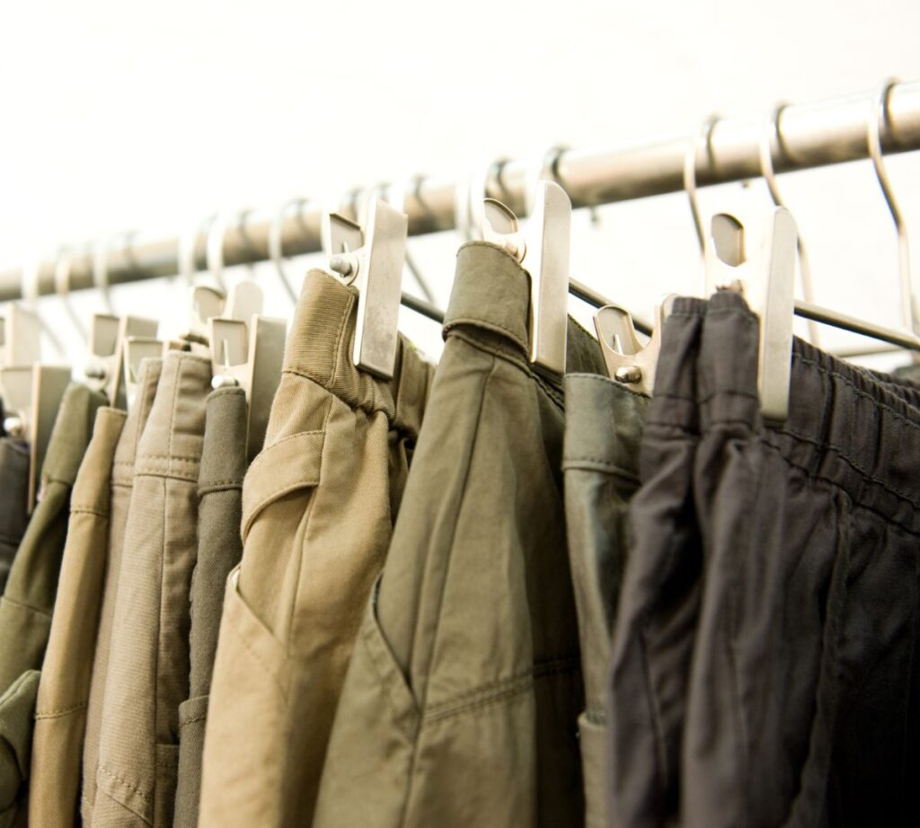 a row of mens trousers on a hanging rail. the trousers are all shades of green.
