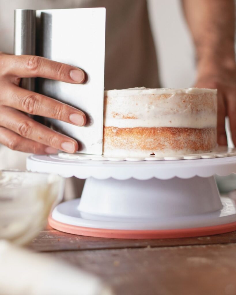 a cake with a thin layer of icing. the baker is using a palette knife to ensure the icing is smooth