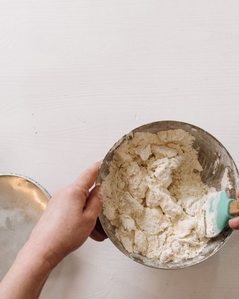 a baker mixing a cake batter, the flour has just been added and is being mixed in with a green spatula