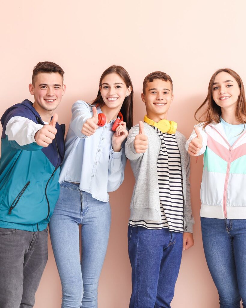 A group of teenagers standing in a group, against a pink wall. showing teenage friendships