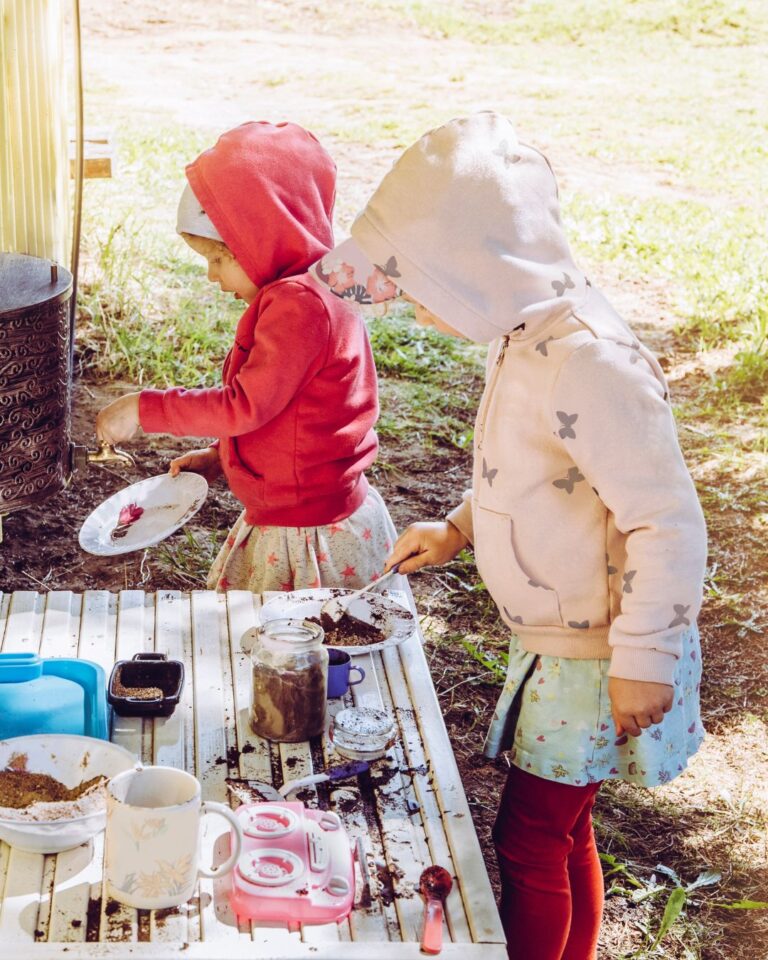 2 little girls outside in winter playing with a mud kitchen having magical playtime fun